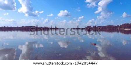 A mesmerizing view of reflective water on the background of trees under the cloudy sky Royalty-Free Stock Photo #1942834447