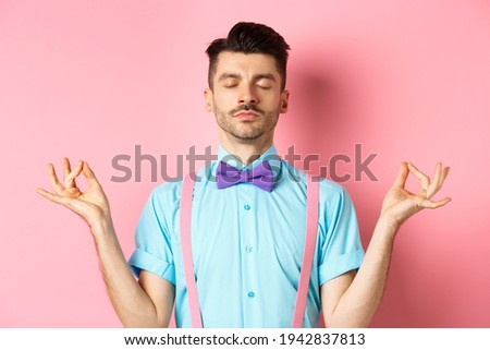 Young guy in bow-tie standing calm and peaceful, meditating with hands in mudra zen gesture and closed eyes, practice yoga to relax, standing over pink background