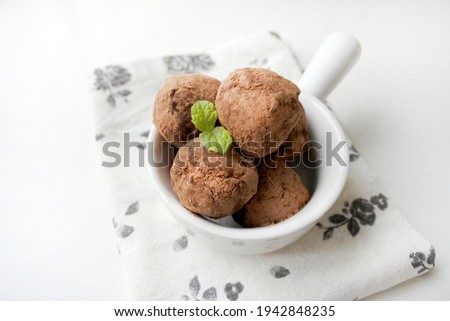 Homemade healthy vegan chocolate truffles with dates, oats, breadcrumb, nuts, cocoa powder and rum. Decorated with mint on white plate on rose pattern napkin on white table background. Horizontal top 
