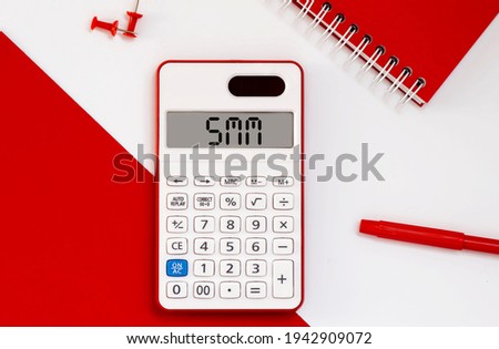 calculator with the word SMM on display with red notepad and office tools