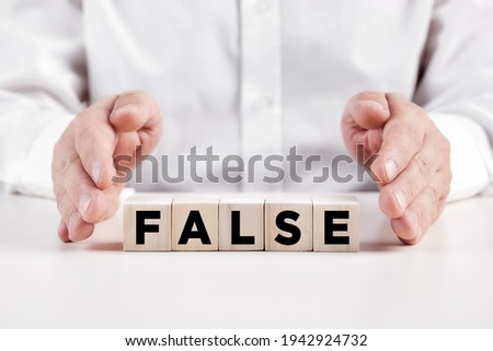 Businessman hands covers the wooden cubes with the word false. Misleading information concept.  Royalty-Free Stock Photo #1942924732