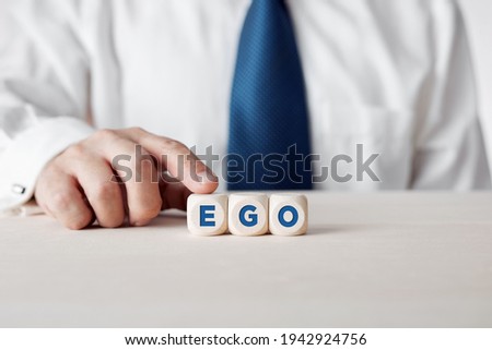 Businessman pressing his finger on the wooden cubes with the word ego. Personal ego, narcissism or selfishness concept.  Royalty-Free Stock Photo #1942924756