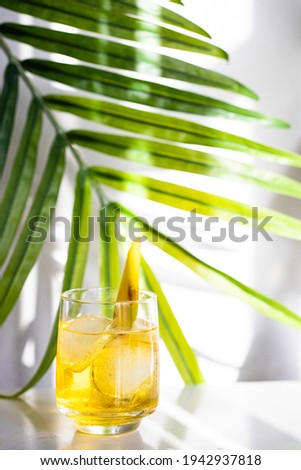 Refreshment cocktail decorated with banana slice garnish on white background with palm leaf . Summer time and vacation concept.