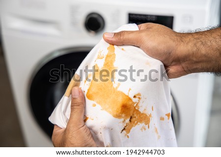 White cotton shirt A lot of stains, stains, coffee stains, man's hand holds the shirt up and spreads it to look dirty Must be brought to the washing machine Royalty-Free Stock Photo #1942944703