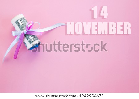 calendar date on pink background with rolled up dollar bills pinned by pink and blue ribbon with copy space. November 14 is the fourteenth  day of the month.