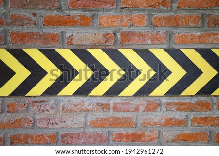 Yellow and black arrow sign background on brick cement wall.