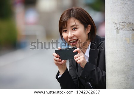 A woman taking a picture with a smartphone from behind a telephone pole 