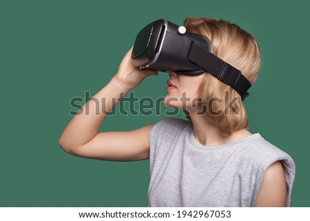 Side view photo of a caucasian woman with blonde hair trying new vr headset on a green studio wall