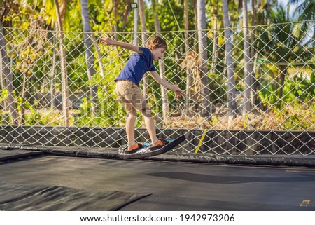 Happy boy on a soft board for a trampoline jumping on an outdoor trampoline, against the backdrop of palm trees. The trampoline board is like a wakeboard, skateboard or snowboard trainer to hone your