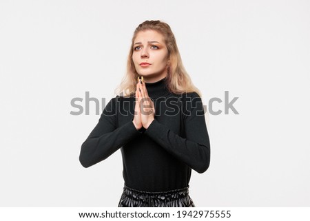 Attractive blonde girl prays in harmony, keeps palms pressed together in praying gesture. Human emotions, gesture concept. Studio shot, white background, isolated