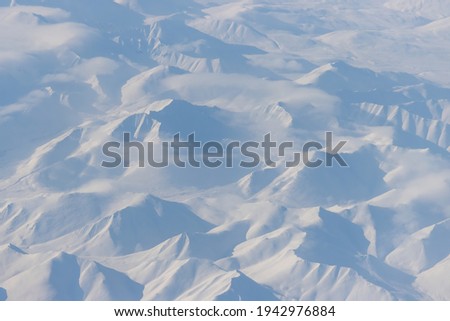 Aerial view of snow-capped mountains and clouds. Winter snowy mountain landscape. Travel to the far north of Russia. Korbendya Range, Kolyma Mountains, Magadan Region, Siberia, Russian Far East.