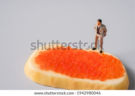  Miniature people, a businessman standing on a caviar sandwich, the concept of wealth and success
