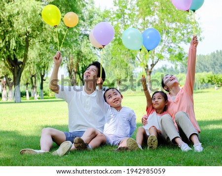 A family of four flying balloons in the park,looking up