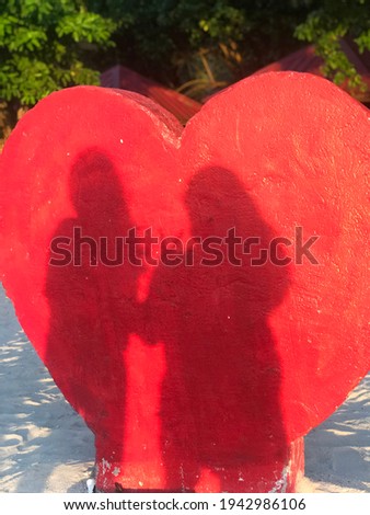 A photo of silhouettes of two women standing in front of a heart.