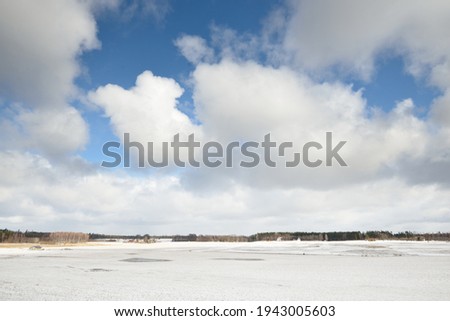 Frozen river on a sunny winter day. Clear blue sky, dramatic clouds. Idyllic rural landscape. Winter wonderland. Nature, seasons, climate change, ecology, ecotourism, Christmas vacations