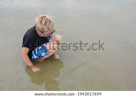 A boy is on the beach at low tide, looking for small fish in the shallow water