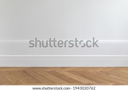 Fragment of classic white interior with wooden french herringbone parquet floor and installed wall panels, decorated with moldings and skirting boards. Final stage of finishing works in the apartment Royalty-Free Stock Photo #1943020762