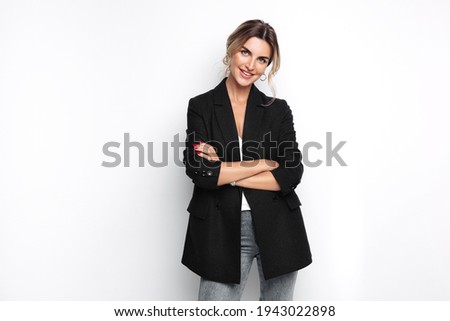Confident young blond woman smiling, looking at camera standing with crossed arms isolated on grey background. Studio portrait of successful friendly female in blazer, posing over white wall. 