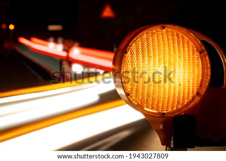 Traffic barring with orange yellow battery flash lights indicating road closure at construction sites, accidents or blocked roads. Passing cars leaving light tracing while long time exposure.