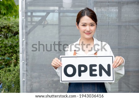 Beautiful Asian woman present banner with word open in front of green house and happy emotion relate with re-open the business with sustainable activity.
