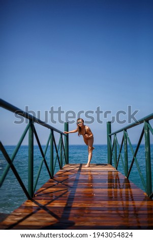 beautiful young woman in a brown swimsuit walks on the pier by the beach on the sea on a summer sunny day