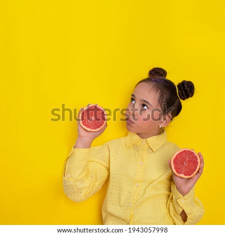 Portrait of a little modern fashion  girl holding a grapefruit on a yellow background for copy space