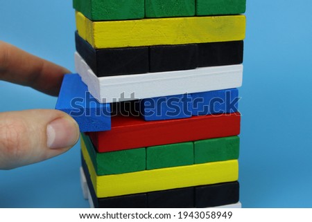 male hand pulls a wooden brick out of the tower on a blue background