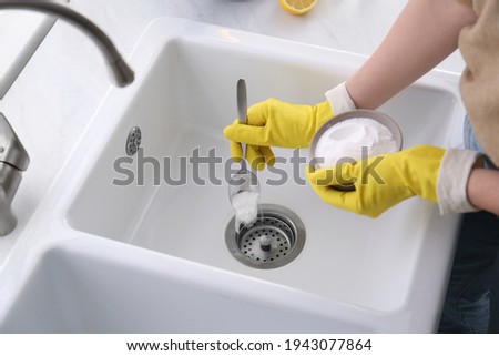 Woman using baking soda to unclog sink drain, closeup Royalty-Free Stock Photo #1943077864