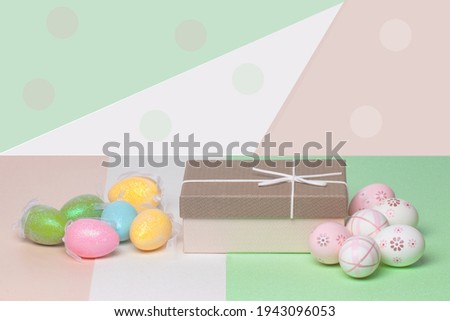 Easter greeting card template. Close-up of colorful eggs and a gift box on a multicolour table against abstract geometrical bright background. Copy space for your text design.