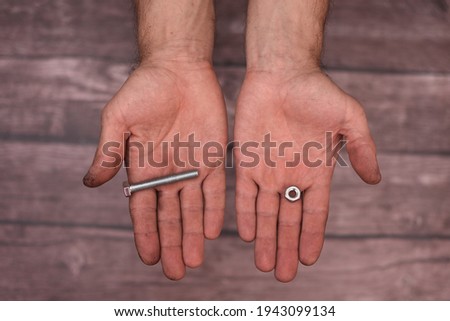 In the men's hands are a bolt and a nut. The man shows the fasteners. Dirty hands.