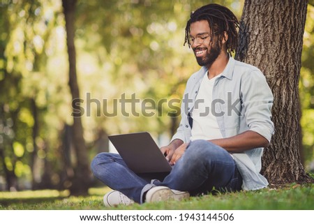 Photo portrait of man in glasses smiling sitting in green park working on laptop smiling Royalty-Free Stock Photo #1943144506