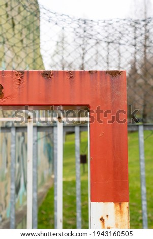 Old rusty football goal on an abandoned sports ground with blurred graffiti and mesh fence. Red white corner close up