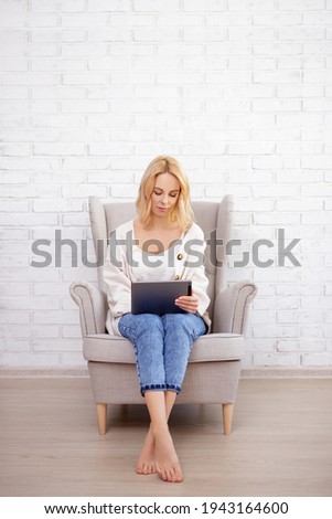 young woman sitting in armchair and using tablet pc - copy space over white brick wall background