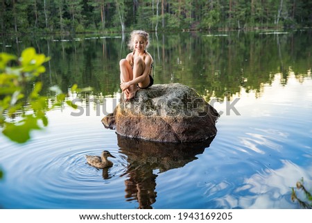 Cute little girl sitting on a rock in lake. Enjoying summer vacation. Child and Nature. Happy isolation concept. Exploring Finland. Scandinavian landscape.  Royalty-Free Stock Photo #1943169205