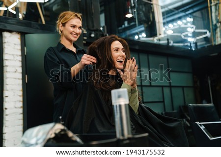 Young smiling woman doing hairstyle for her client in beauty salon
