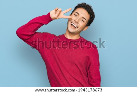 Young handsome man wearing casual clothes doing peace symbol with fingers over face, smiling cheerful showing victory 