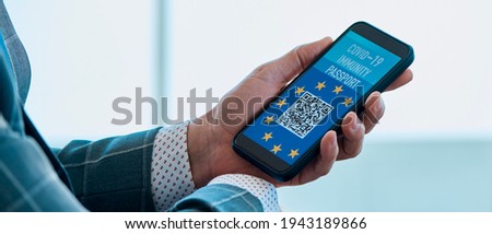 businessman, in the waiting hall of an airport, has a simulated electronic european covid-19 immunity passport in the screen of his smartphone, in a panoramic format to use as web banner or header