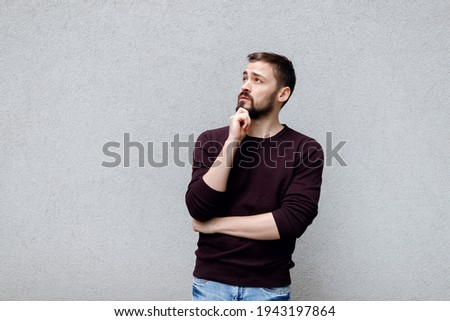 Curious and questioned handsome businessman trying solve problem thinking standing in thoughtful pose rubbing beard making decision against gray background