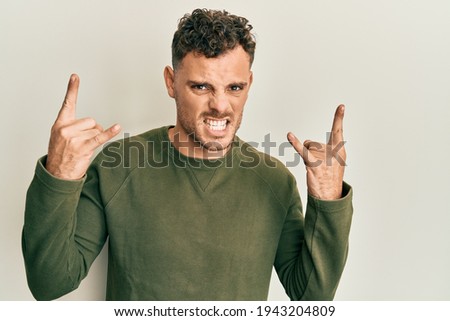 Young hispanic man wearing casual clothes shouting with crazy expression doing rock symbol with hands up. music star. heavy concept. 