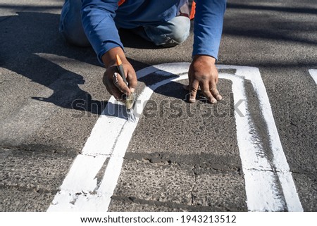 The worker is leaning with his hand to paint the signs on the street.