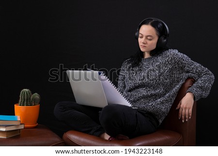 Focused young freelance woman sitting with laptop and headphones, working remotely online from home.