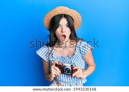 Young beautiful caucasian girl holding vintage camera afraid and shocked with surprise and amazed expression, fear and excited face. 