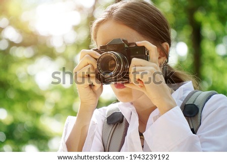 Young woman hiking in forest and taking pictures with old camera                        