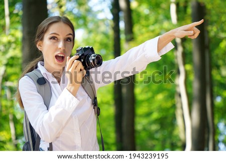 Cheerful woman in the forest takes photos with camera and is enthusiastic about the great motifs                            