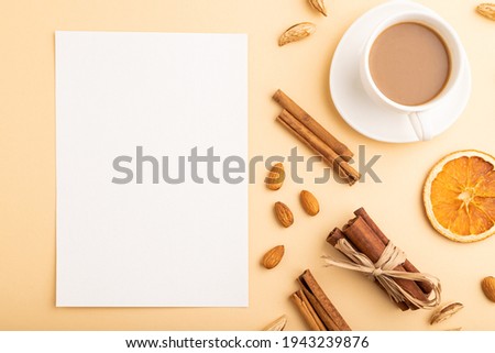 Composition with white paper sheet, almonds, cinnamon and cup of coffee. mockup on orange background. Blank, flat lay, top view, still life, copy space.
