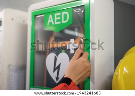Action of a medic rescue staff is opening AED station box to take the AED machine, using to help a heart attack patients. Health care and medical action photo. Selective focus on people's hand. Royalty-Free Stock Photo #1943241685