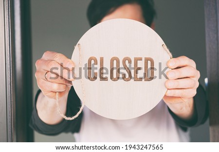Man holds the wooden sign with text: Closed