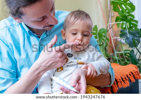Father rubbing pain relieving gel into his little baby boy's growing teeth or gums.  Baby healthcare concept. Royalty-Free Stock Photo #1943247676