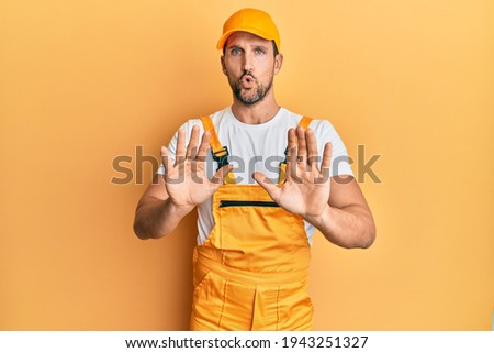 Young handsome man wearing handyman uniform over yellow background moving away hands palms showing refusal and denial with afraid and disgusting expression. stop and forbidden. 