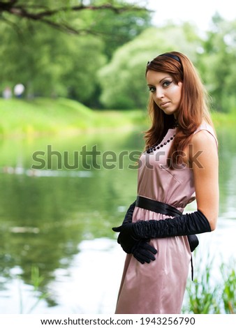 Portrait of young woman with hairstyle in elegant vintage dress near the river.
